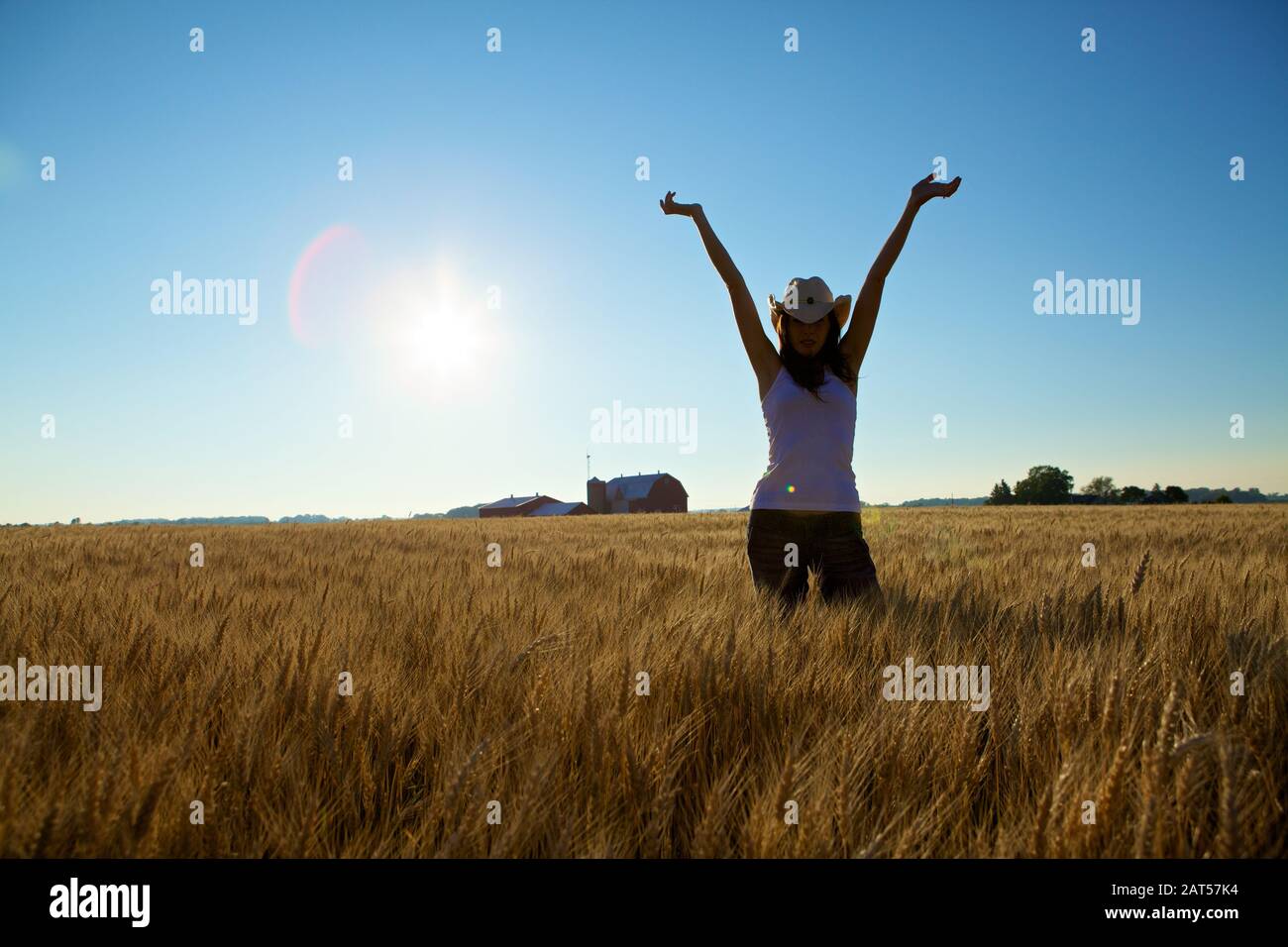 Cowgirl nel campo con le braccia tenute in alto e un fienile in background Foto Stock