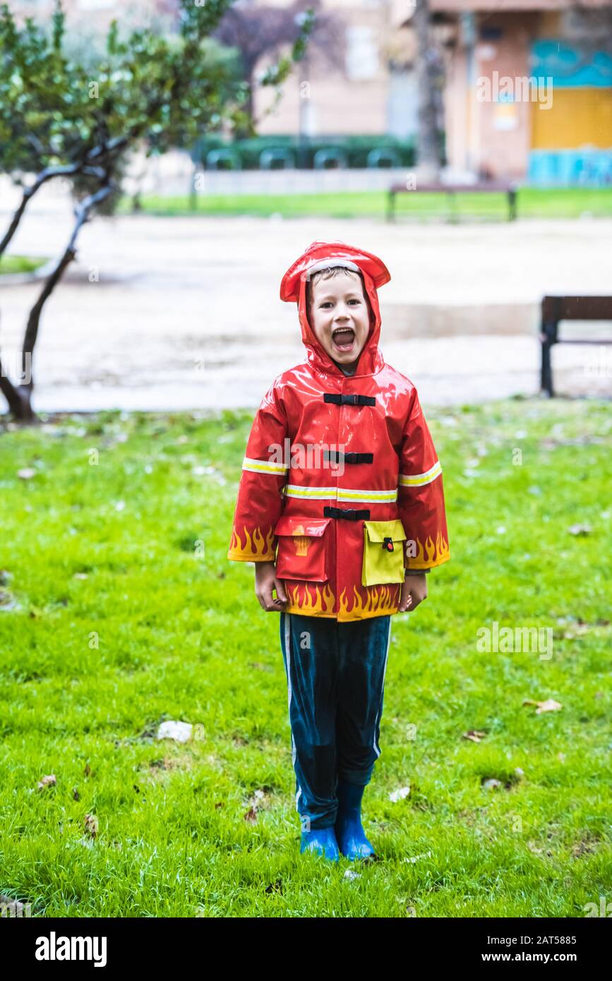 Ragazzo vestito come un pompiere con impermeabile rosso schizza sull'erba  di un parco una giornata piovosa Foto stock - Alamy