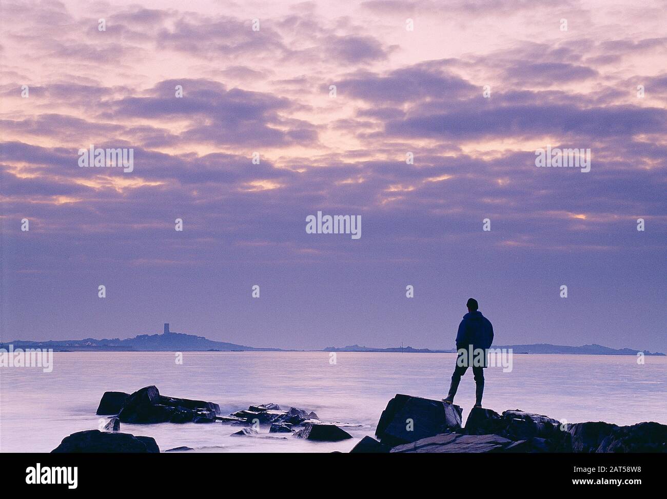 Isole Del Canale. Guernsey. Vista posteriore di un uomo solitario in riva al mare. Vista distante della Torre di Fort Saumarez martello a l'Erée Point. Foto Stock