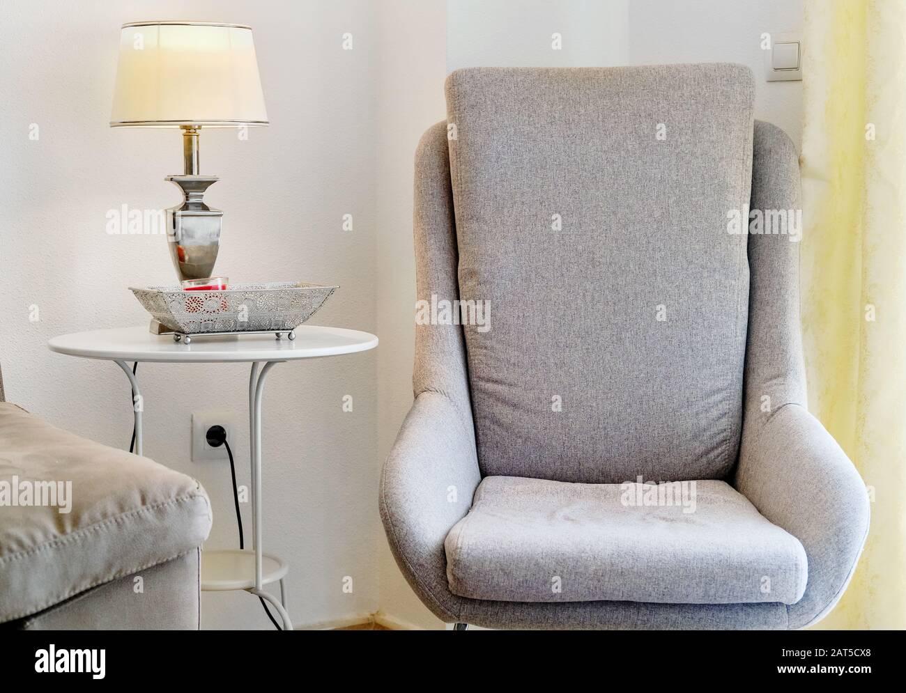 Moderna e intima poltrona di colore grigio all'interno di un grazioso soggiorno luminoso Foto Stock