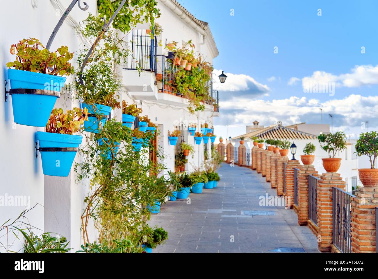 Scenario idilliaco vuoto pittoresca strada di piccolo villaggio bianco-lavato di Mijas. Percorso decorato con piante pendenti in fioriere blu luminoso Spagna Foto Stock