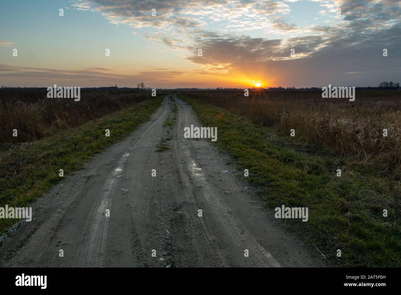 Strada sterrata lunga e dritta e tramonto Foto Stock