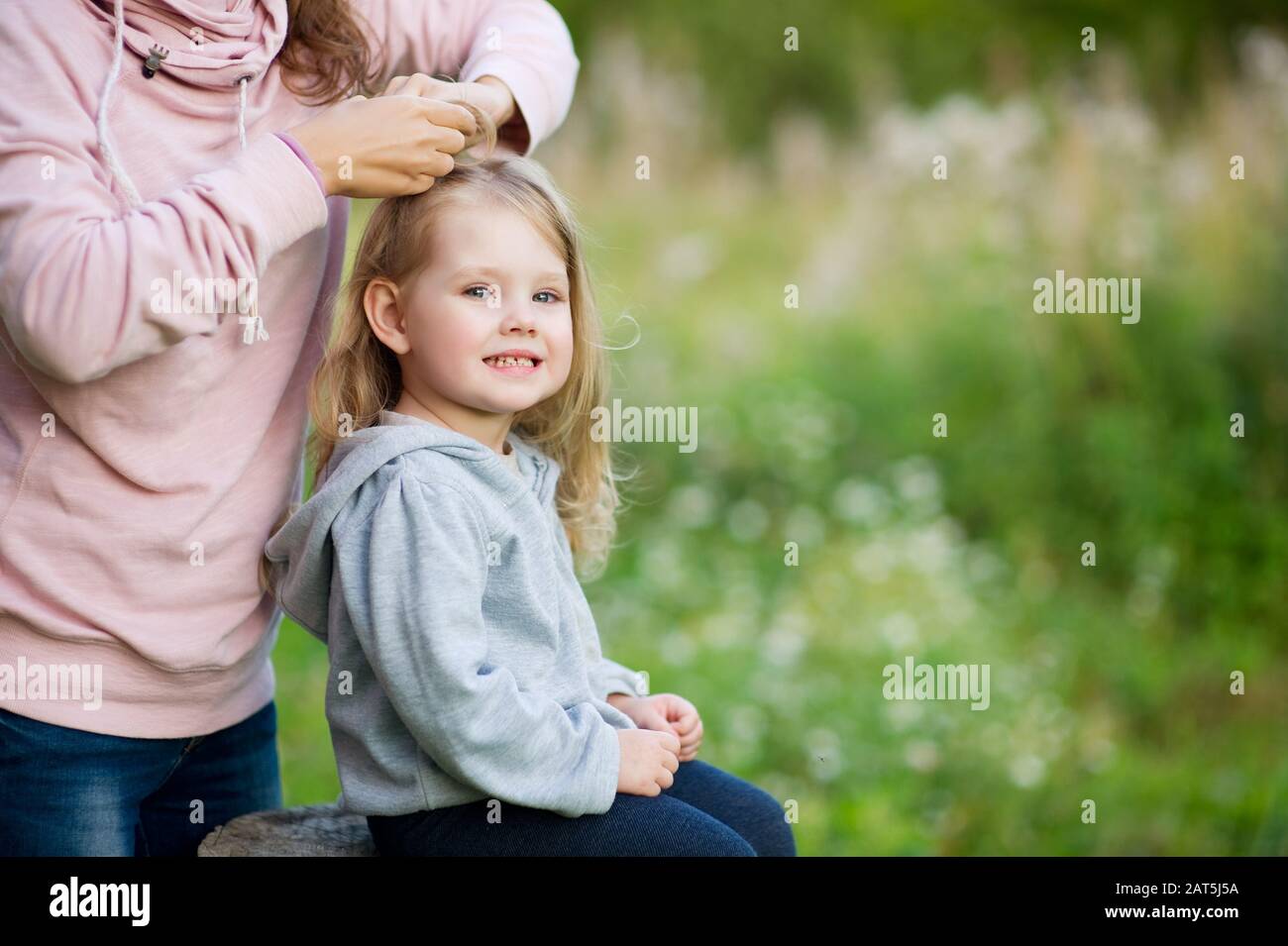 Una ragazza siede su un moncone e la mamma la tesserà una pigtail Foto Stock