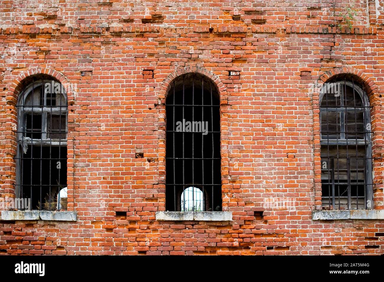 muro di mattoni di una vecchia prigione abbandonata con bar sulle finestre Foto Stock