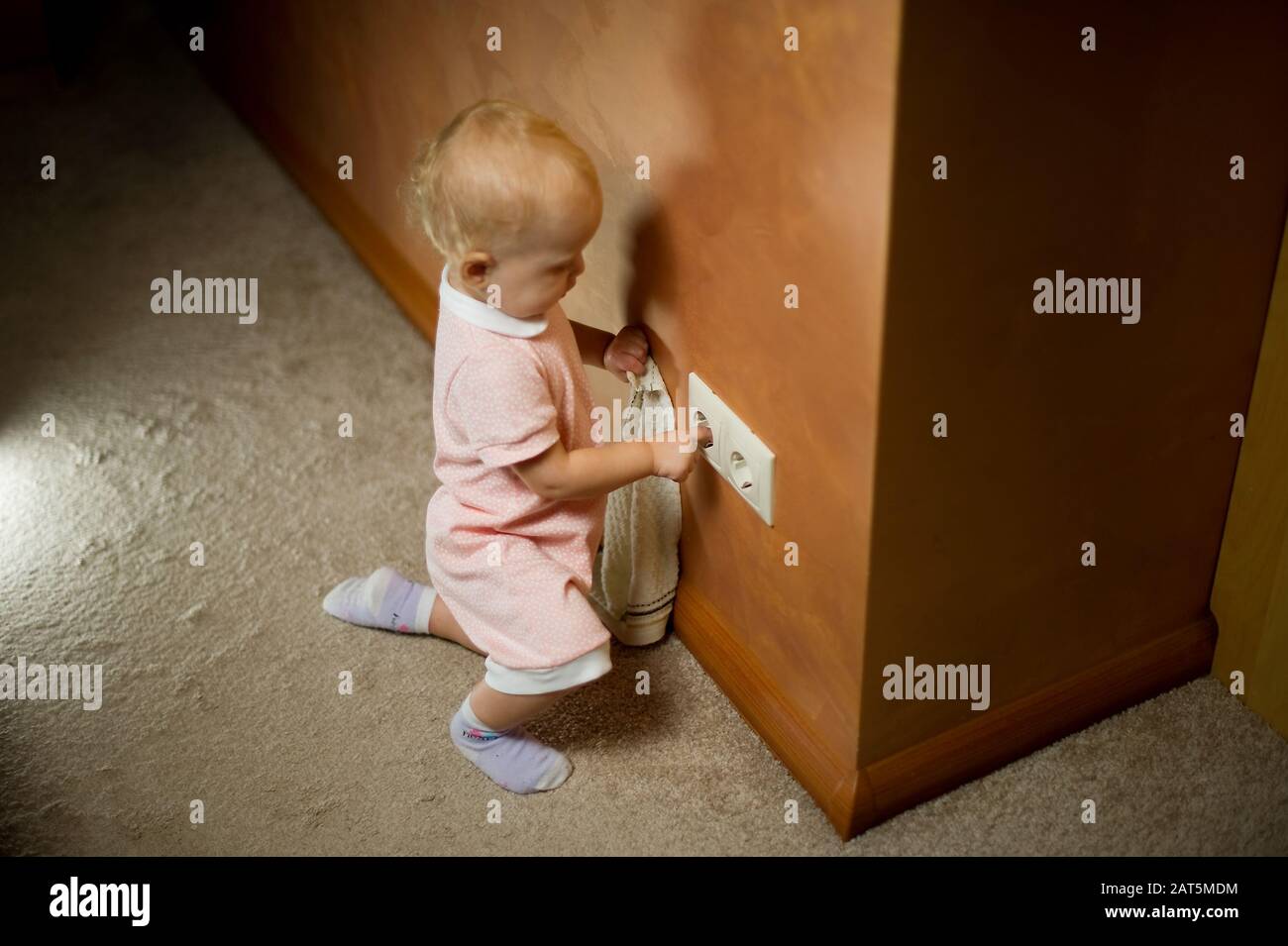 Bambino che gioca con la presa elettrica sul pavimento a casa. Un bambino che cerca di entrare nelle prese elettriche Foto Stock