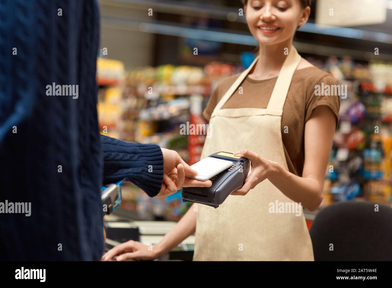 Shopping Giornaliero. Uomo in piedi al banco del supermercato pagare per gli acquisti con smartphone Contactless primo piano cassiere sorridente allegro Foto Stock