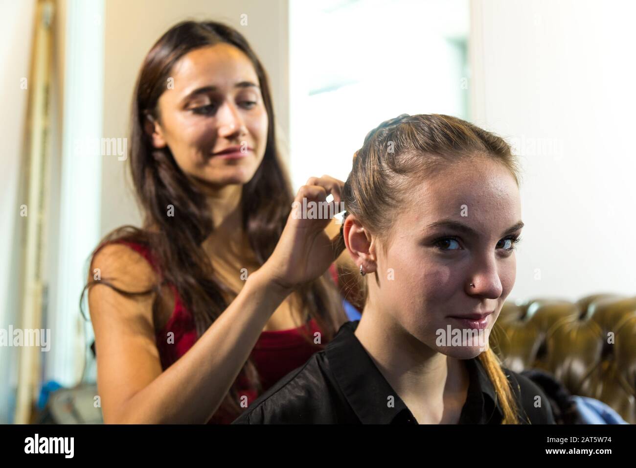 Giovane donna indiana che trita i capelli della donna caucasica. Scatto medio. Guardando la fotocamera. Foto Stock