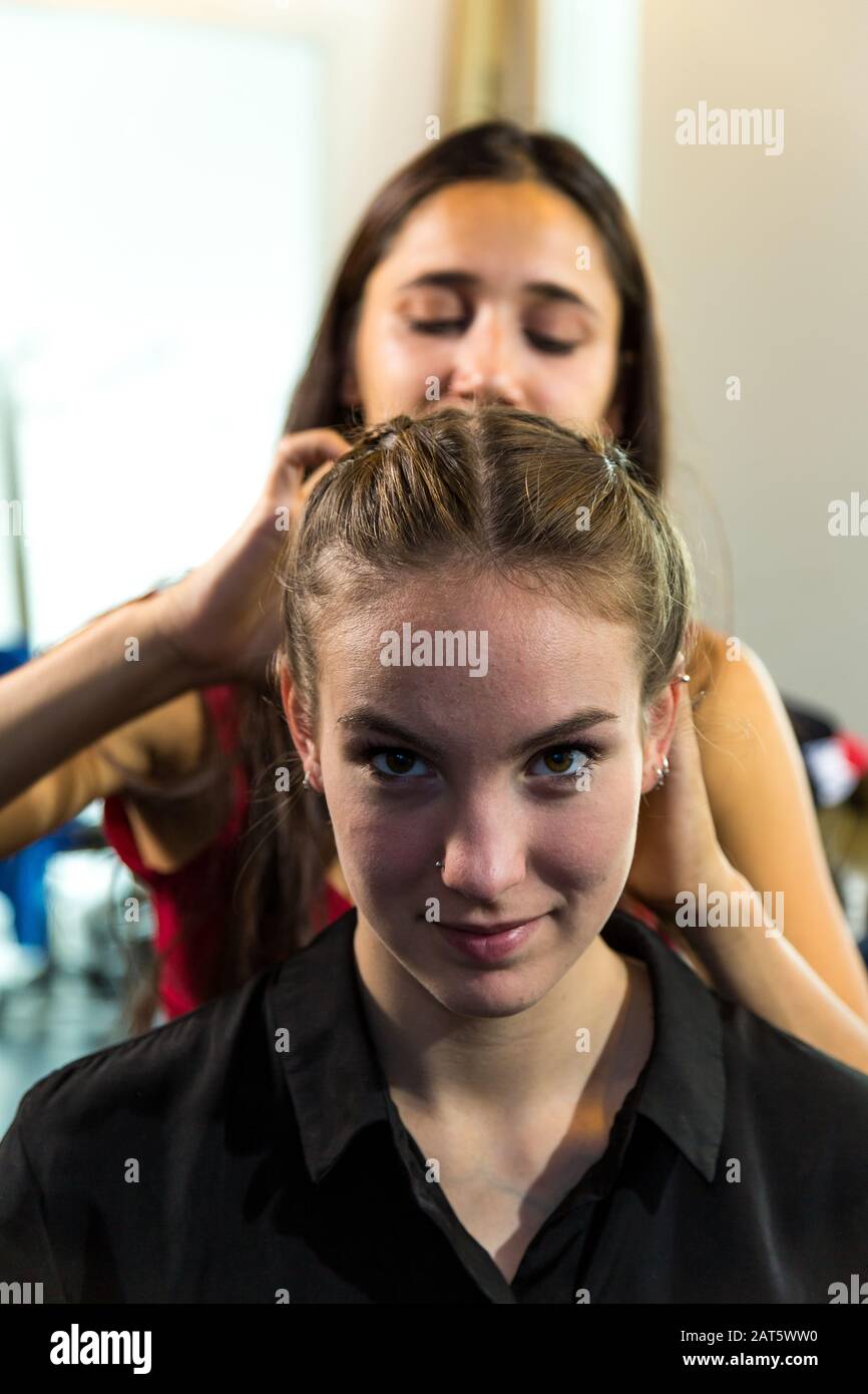 Giovane donna che guarda la macchina fotografica che ottiene i capelli intrecciati. Scatto medio. Foto Stock