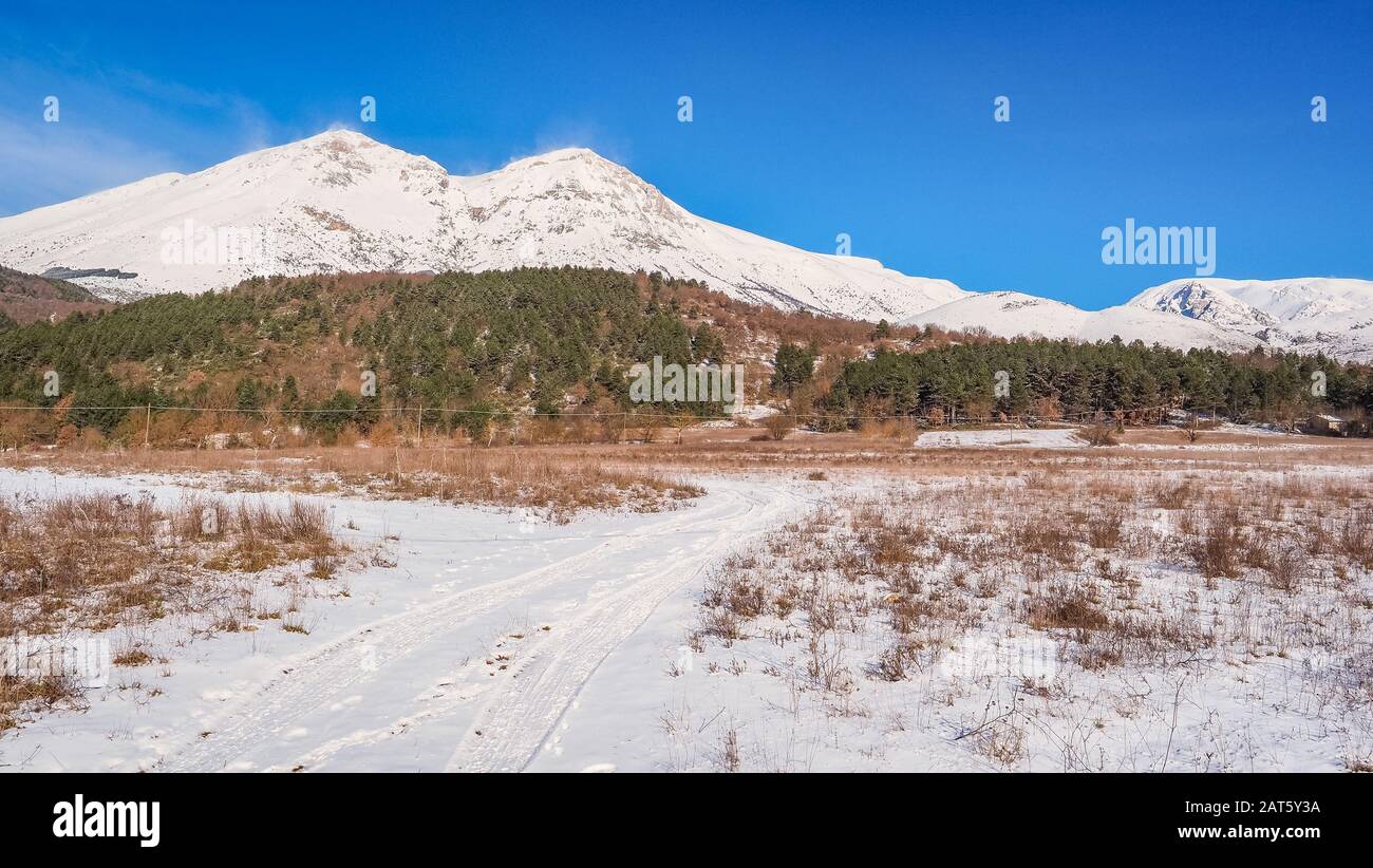 Paesaggio invernale con sentiero innevato e cime del monte Velino in lontananza. Località nei pressi della città di massa d'Albe, l'Aquila, Italia, parte dell'Appennino abruzzese. Foto Stock
