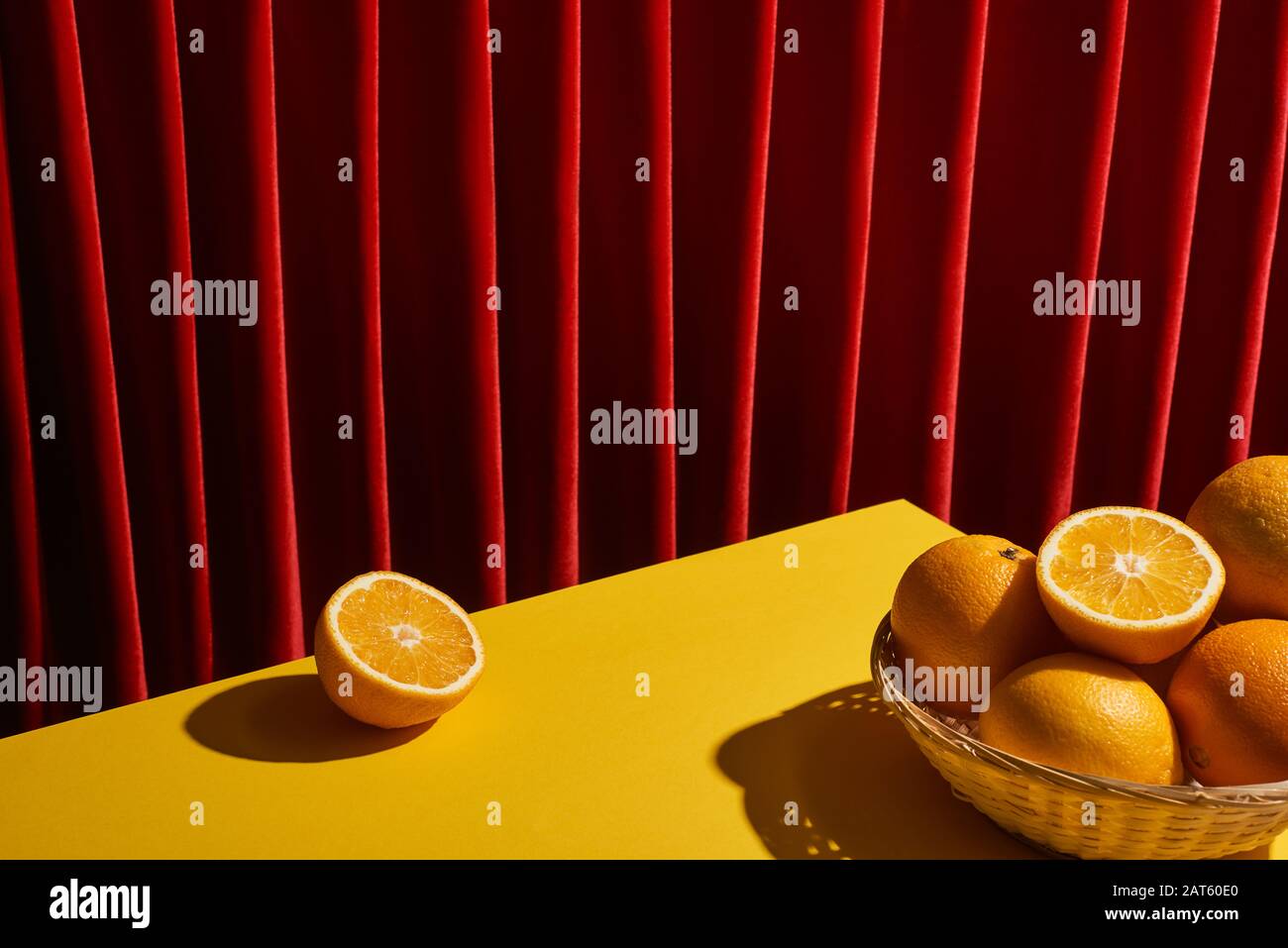 classica ancora vita con arance in cesto di vimini sul tavolo giallo vicino tenda rossa Foto Stock