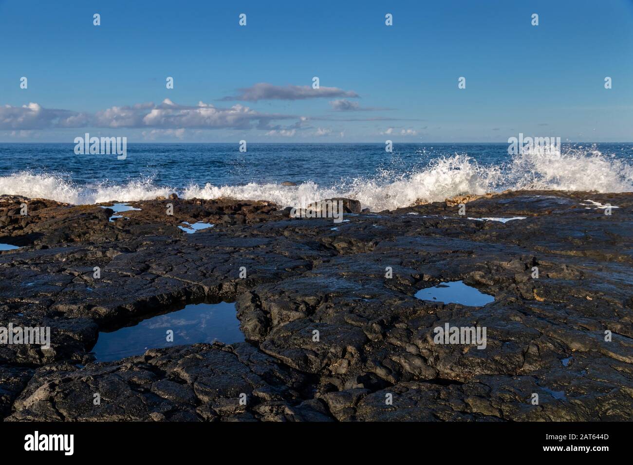 Spiaggia hawaiana sulla costa occidentale di Kona; roccia vulcanica nera con piscine di marea; onde oceaniche che si infrangono al bordo dell'oceano. Foto Stock