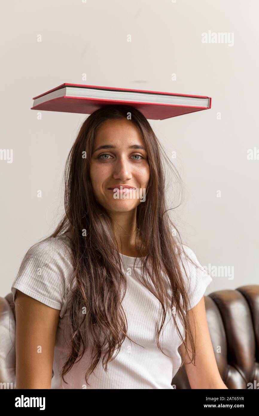 Ritratto di giovane donna con libro sulla testa. Scatto medio. Guardando la fotocamera. Foto Stock