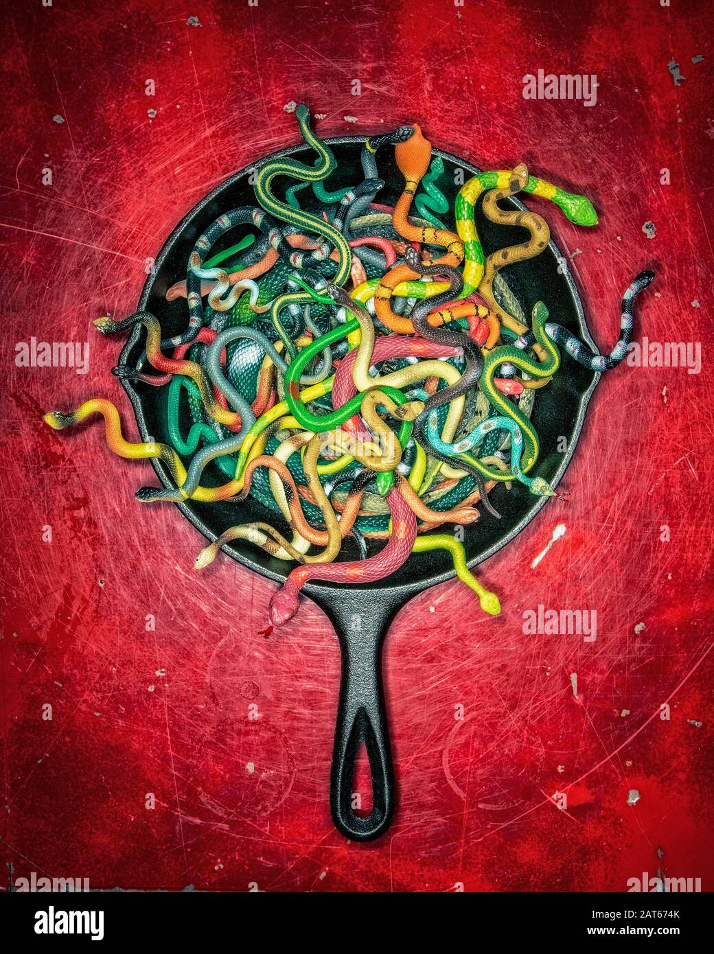 Una moltitudine di serpenti colorati di gomma che squirming in una padella di ferro contro uno sfondo rosso profondo Foto Stock