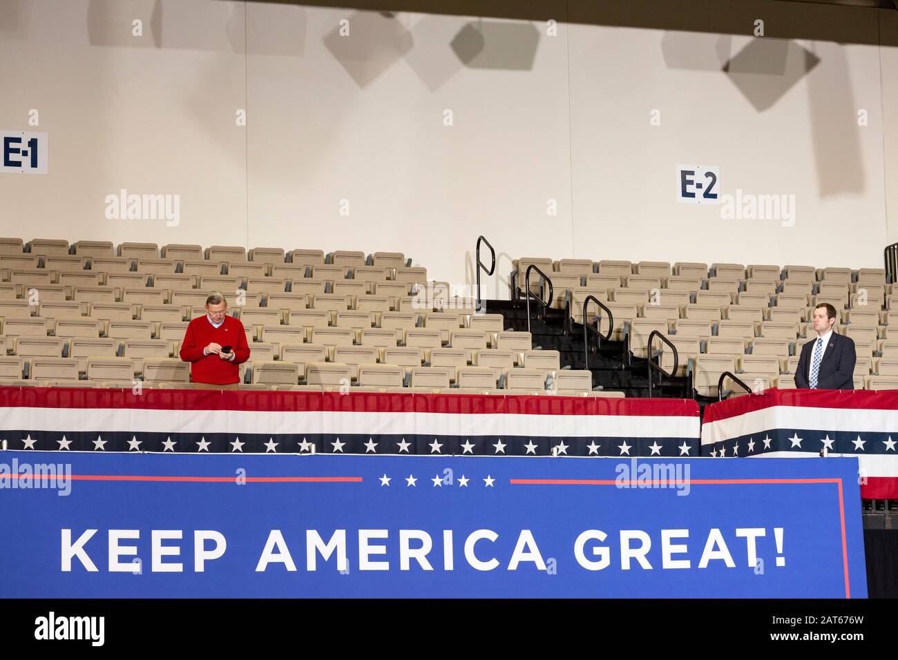 Uomo in un'area a sedere vuota con il telefono cellulare monitorato dalla sicurezza ufficiale quando la folla entra a sedere al rally 'Keep America Great' Foto Stock