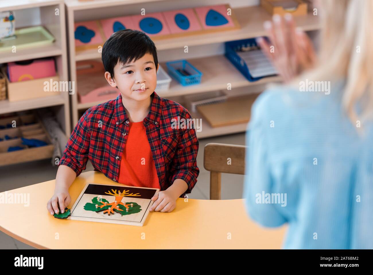 Fuoco selettivo del capretto asiatico che guarda l'insegnante nella scuola di montessori Foto Stock