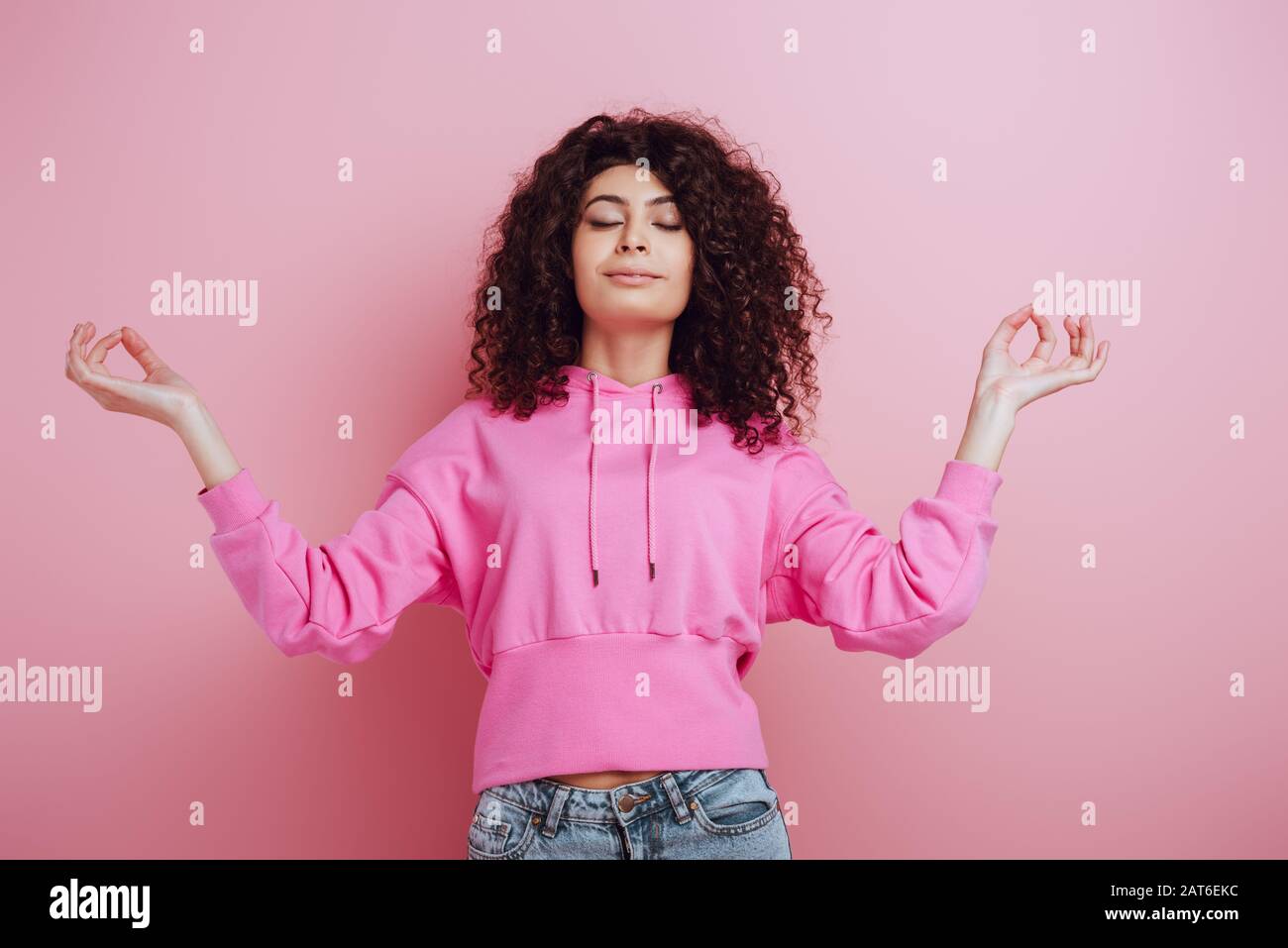 bella ragazza bi-razziale meditando con gli occhi chiusi mentre in piedi su sfondo rosa Foto Stock