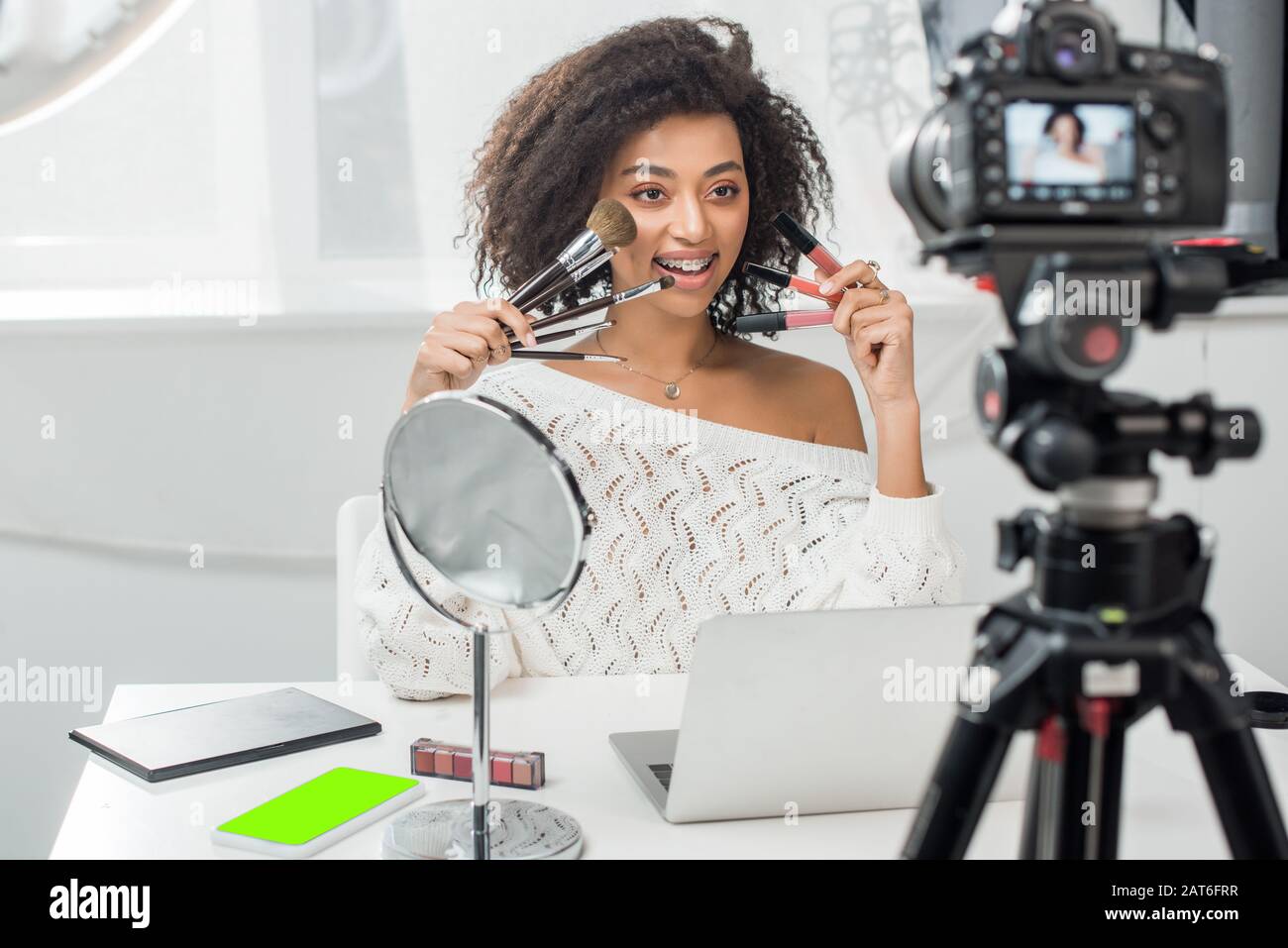 focus selettivo di happy african american influencer in bretelle che tengono  le perdite di labbro e pennelli cosmetici vicino smartphone con schermo  verde e digitale Foto stock - Alamy