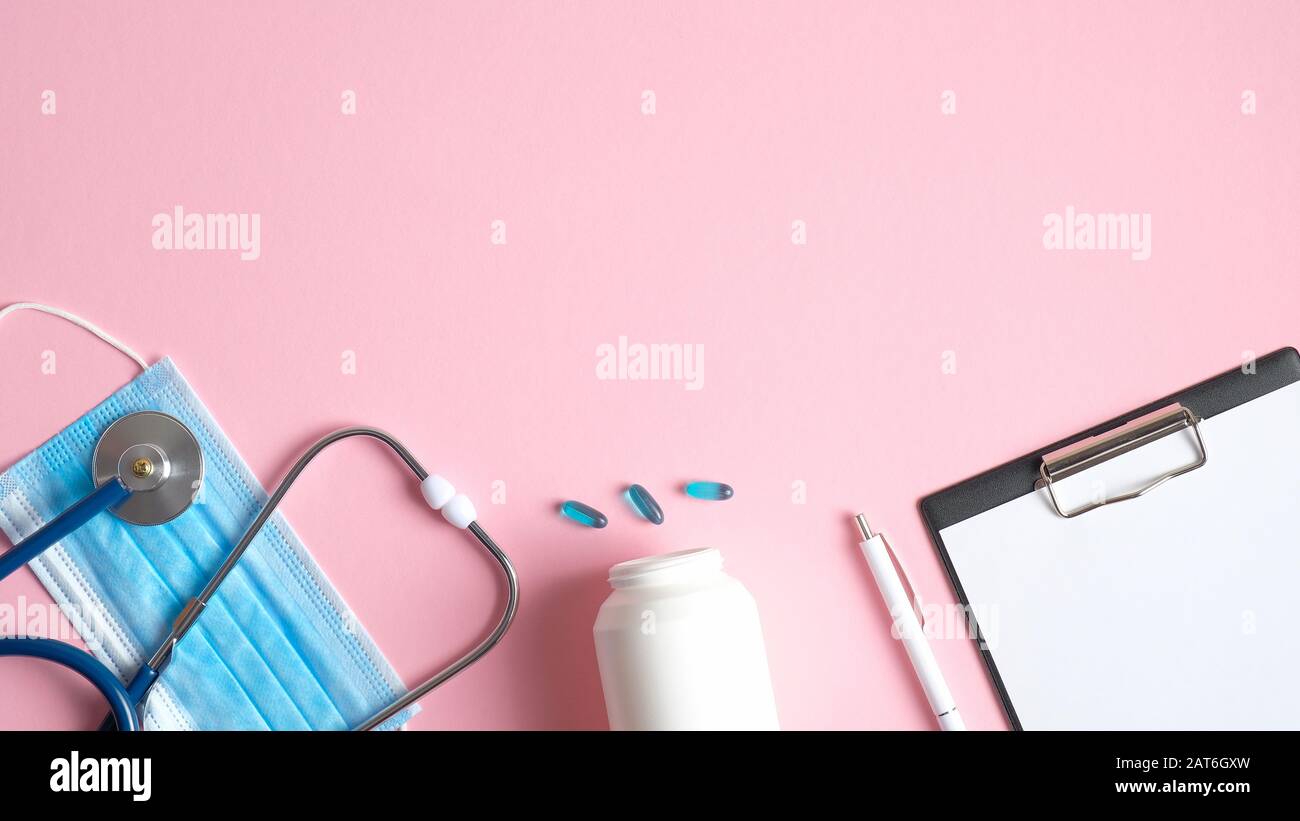 Apparecchiature mediche su sfondo rosa. Maschera chirurgica a posa piatta, stetoscopio, pillole, appunti medici e penna. Vista dall'alto tabella medici. Sanità e me Foto Stock