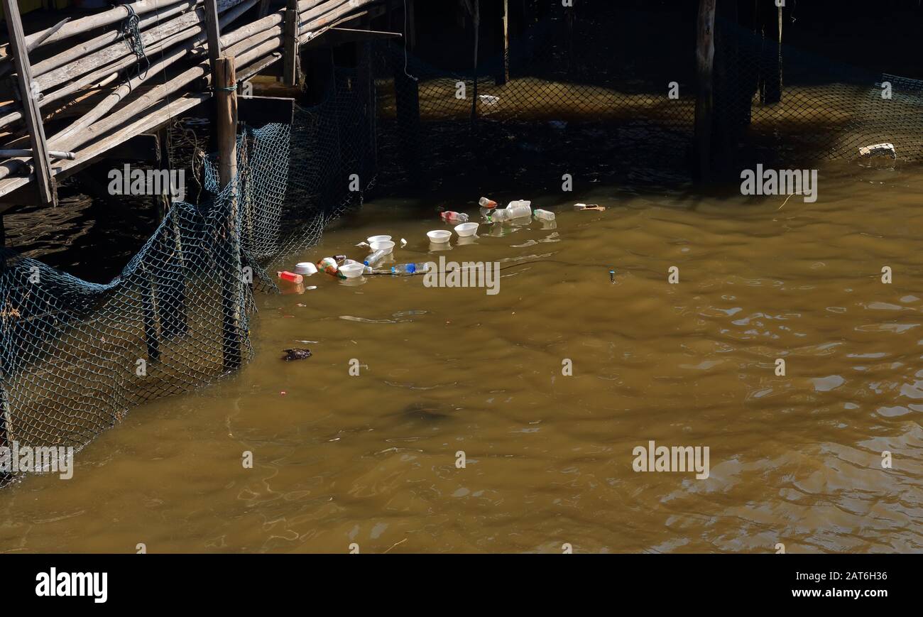 Bottiglie di plastica e contenitori di alimenti in schiuma buttati via nel fiume vicino alla rete legata alla struttura in legno sul lungomare, concetto di cambiamento climatico Foto Stock