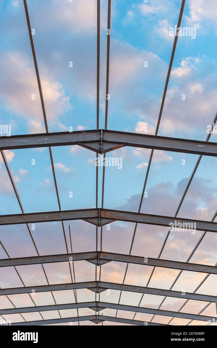 Vista ad angolo basso del bellissimo cielo blu nuvoloso, come si vede sotto il disegno geometrico dei telai in metallo del tetto Foto Stock