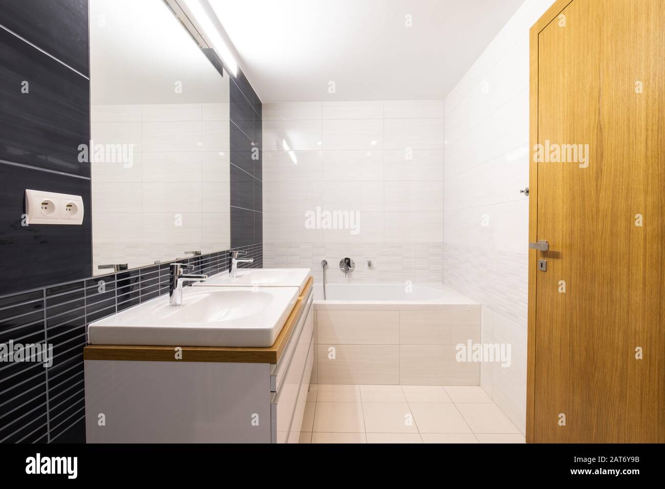 bagno moderno con grande specchio e due lavandini, vasca e porta in legno Foto Stock