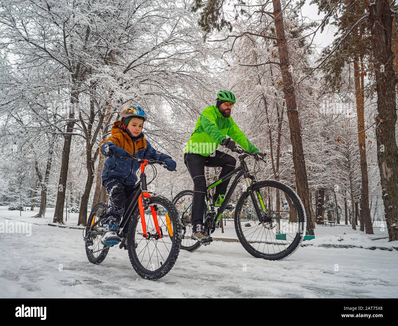 Un padre e suo figlio cavalcano una bicicletta in un parco invernale. Fine settimana in un parco innevato Foto Stock