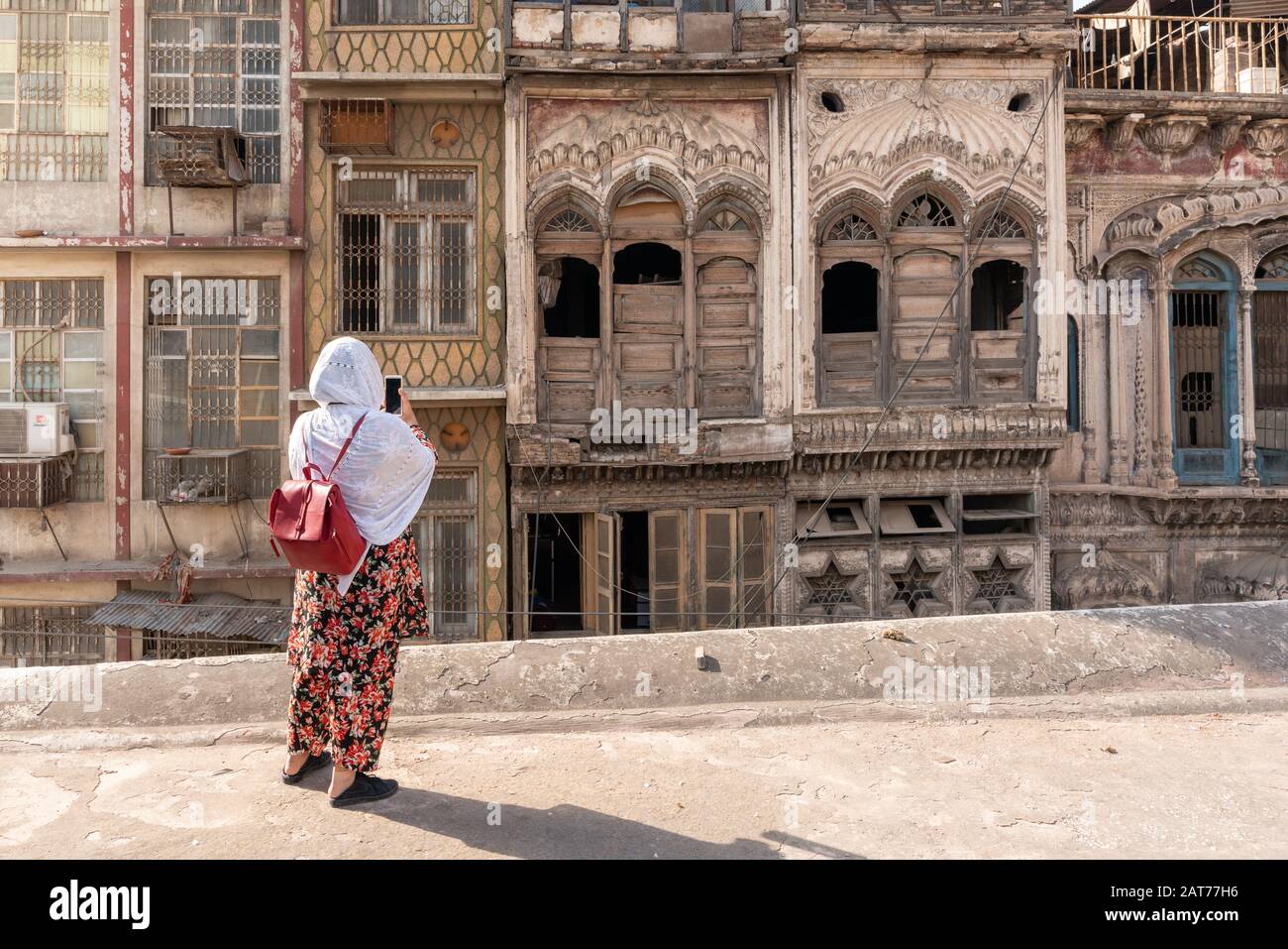 Ragazza pakistana in salwar floreale kameez utilizzando il telefono cellulare per scattare una foto di legno haveli Mansion finestre a Peshawar, Pakistan Foto Stock