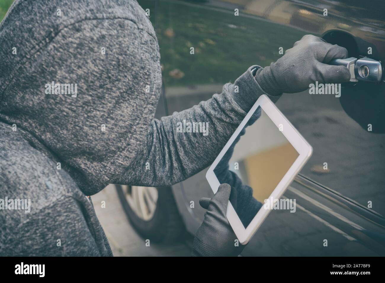 Incappucciati ladro tenta di rompere l'auto di sistemi di sicurezza con la compressa. Hacking moderno concetto di auto Foto Stock