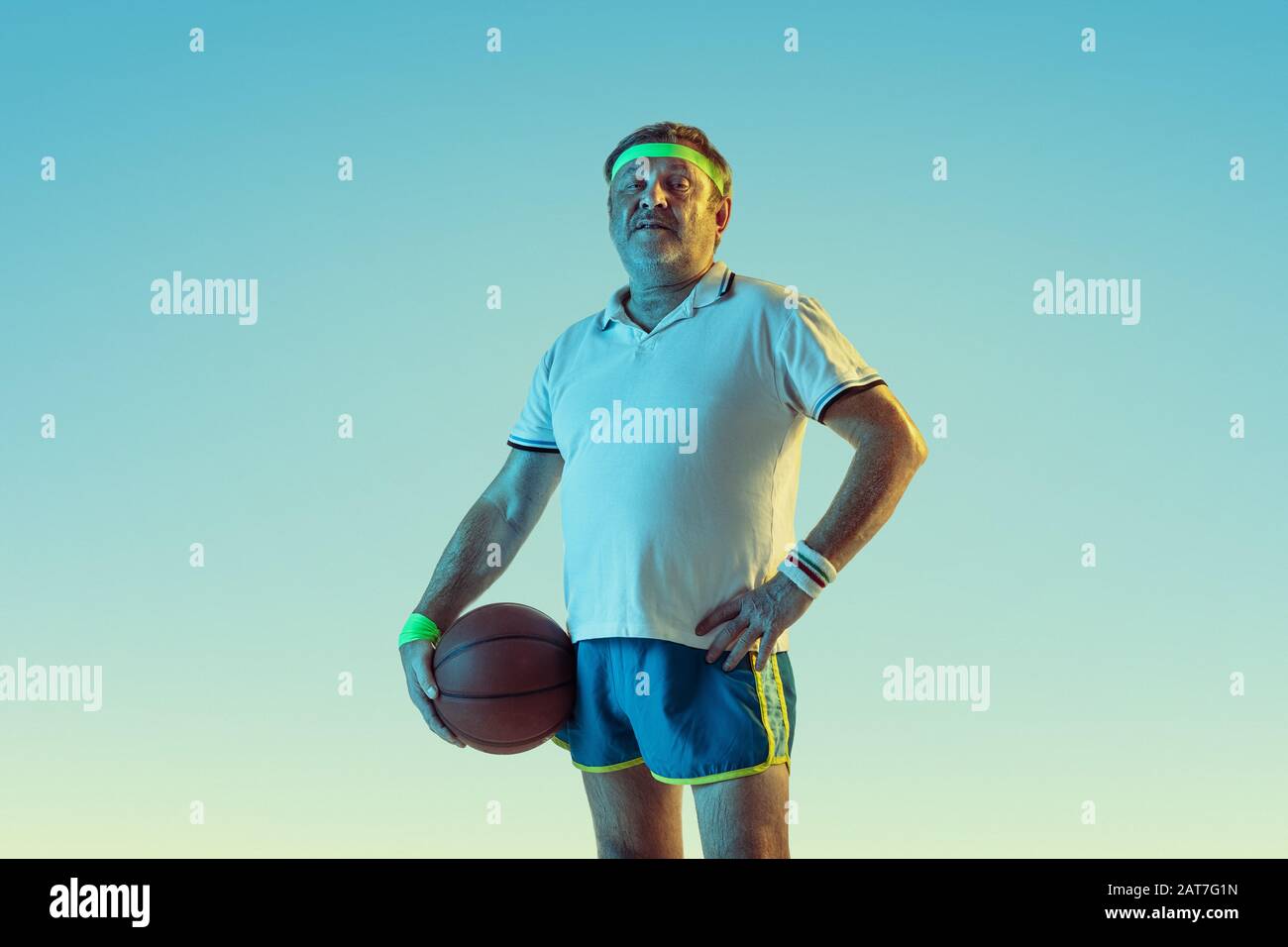 Uomo anziano che gioca a basket su sfondo gradiente in luce al neon. Il modello maschio caucasico in grande forma rimane attivo, sporitivo. Concetto di sport, attività, movimento, benessere, stile di vita sano. Foto Stock