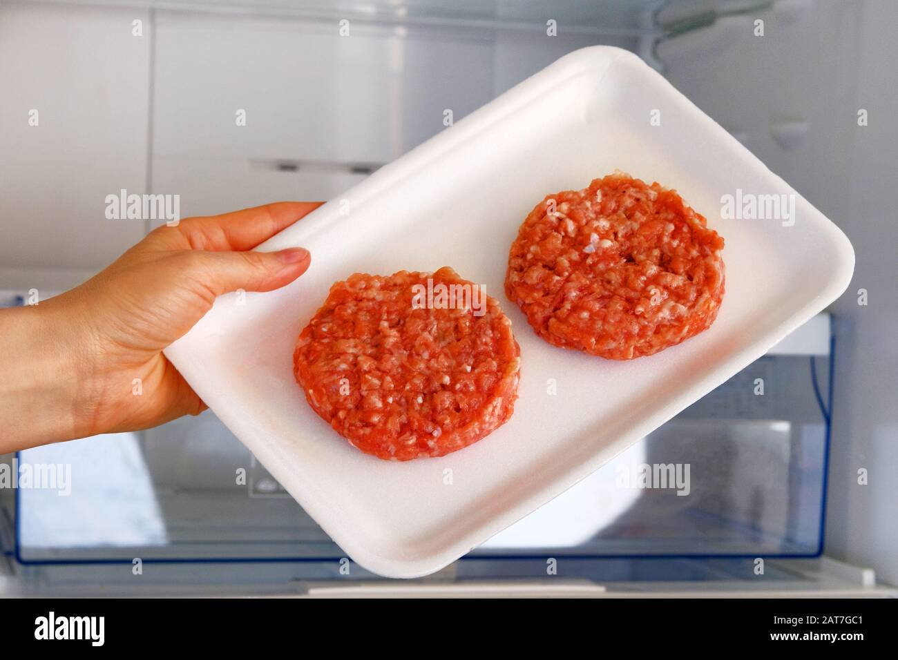 Hamburger di pollo crudo in contenitore è a scaffale in frigorifero aperto. Ingrediente per cucinare piatti di carne. Carne cruda. Foto Stock