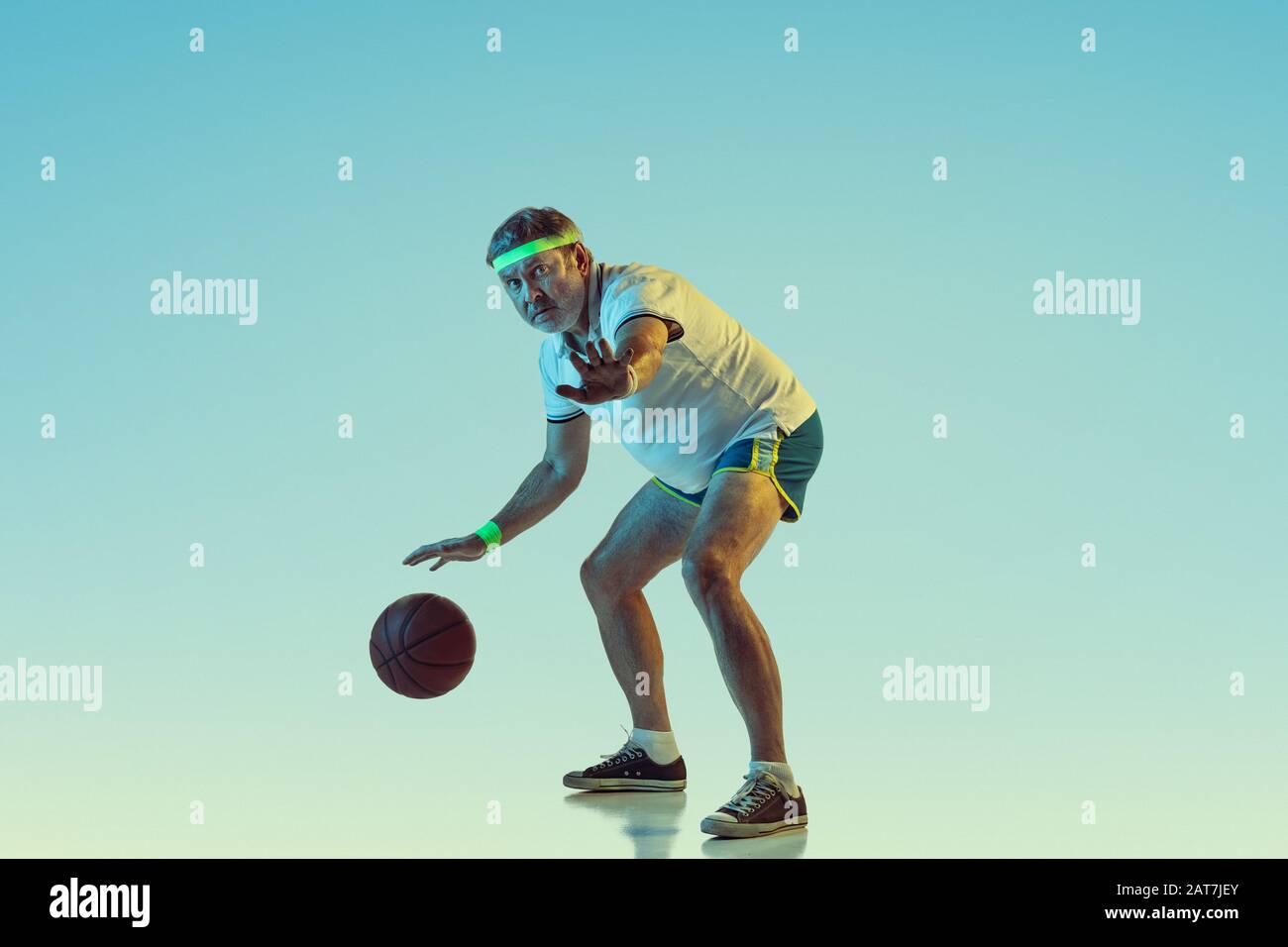 Uomo anziano che gioca a basket su sfondo gradiente in luce al neon. Il modello maschio caucasico in grande forma rimane attivo, sporitivo. Concetto di sport, attività, movimento, benessere, stile di vita sano. Foto Stock