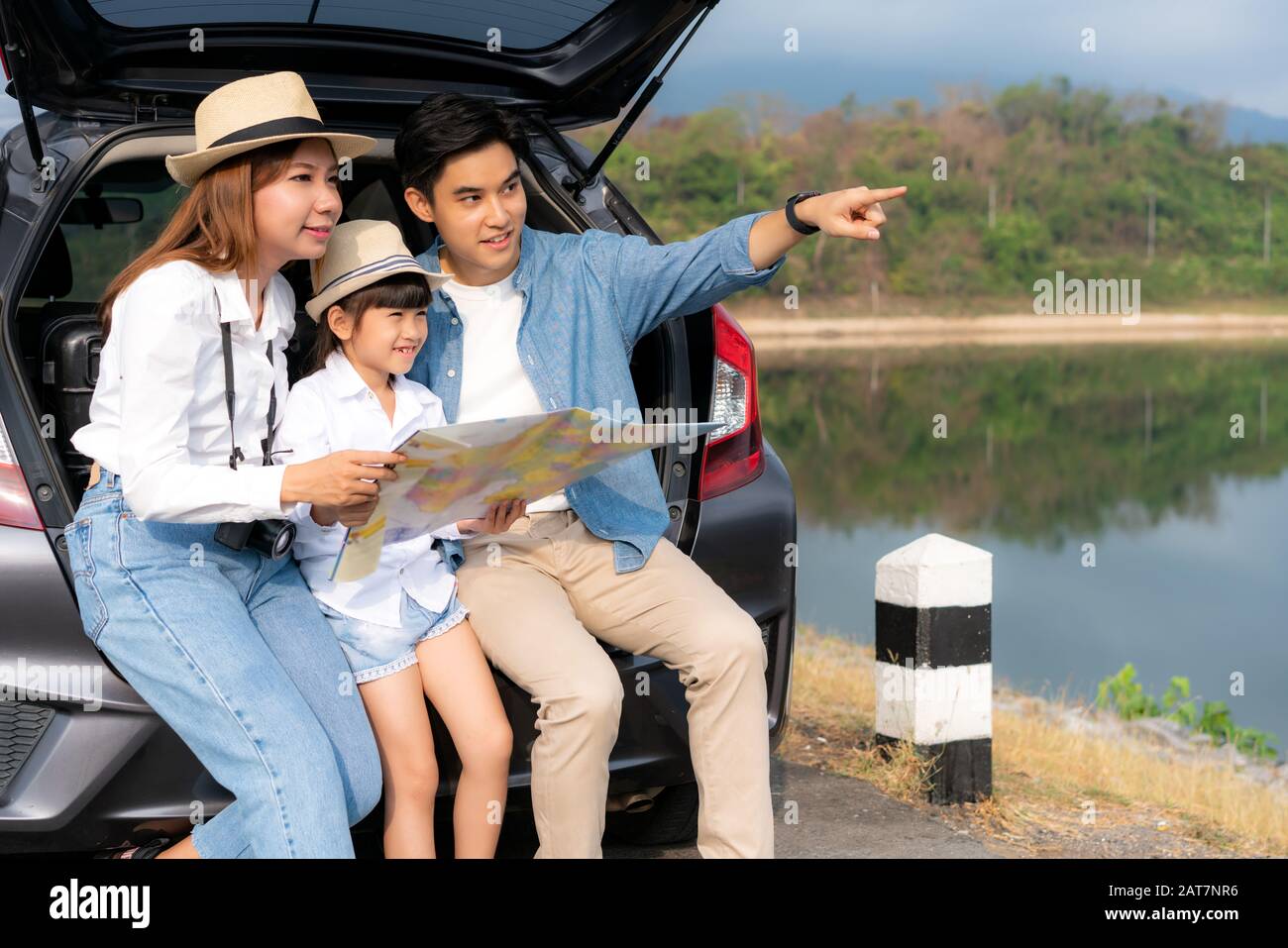 Ritratto della famiglia asiatica seduto in auto con il padre che punta a vedere e madre con figlia che guarda bello paesaggio e tenendo mappe mentre vacat Foto Stock