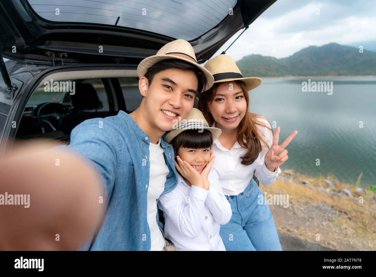 Ritratto di famiglia asiatica seduto in auto con padre, madre e figlia selfie con vista lago e montagna da smrtphone, mentre vacanza insieme in ho Foto Stock