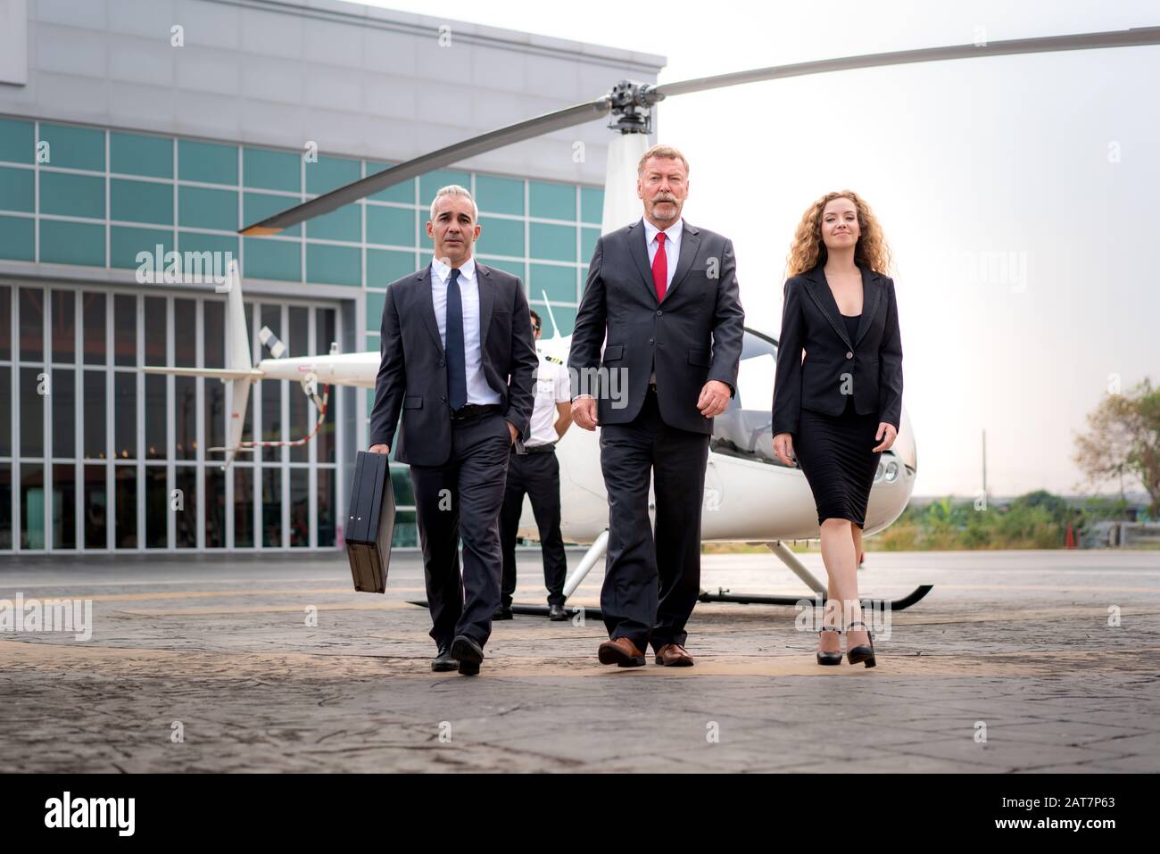 Tre Uomini D'Affari e businesswoman manager con Briefcase a piedi da elicottero quando arriva destinazione a eliporto in aeroporto con elicottero AN Foto Stock
