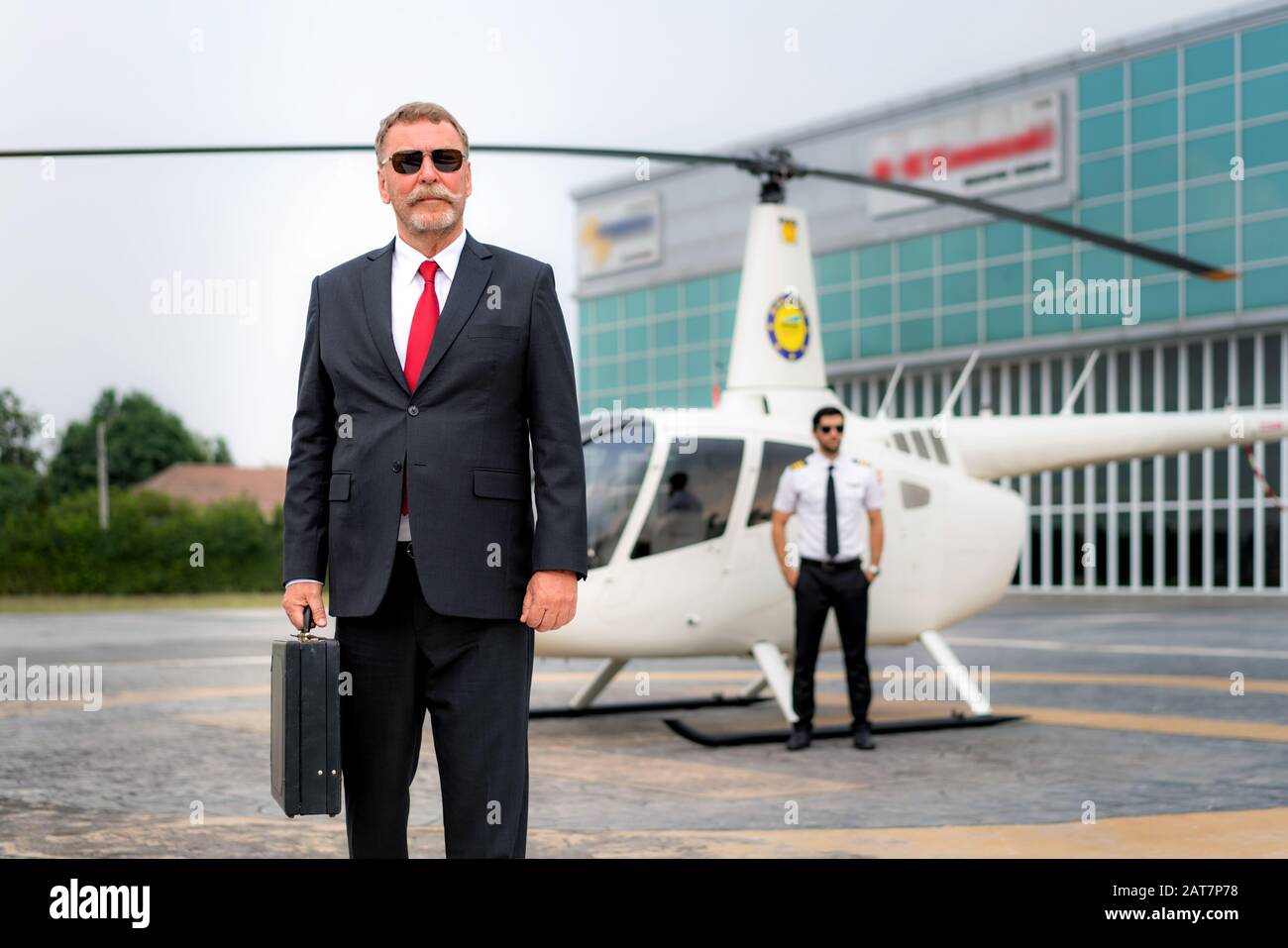 Uomo D'Affari anziano manager con Briefcase a piedi da elicottero quando arriva a destinazione di eliporto in aeroporto con elicottero e capitano standi Foto Stock