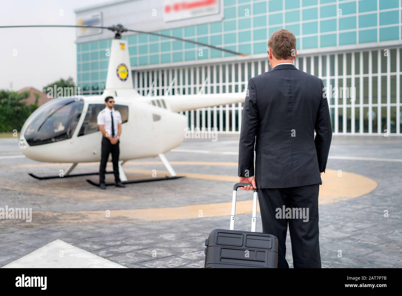 Uomo D'Affari anziano manager con bagagli a piedi per l'elicottero alla partenza per la destinazione a eliporto in aeroporto con elicottero e capitano in piedi Foto Stock