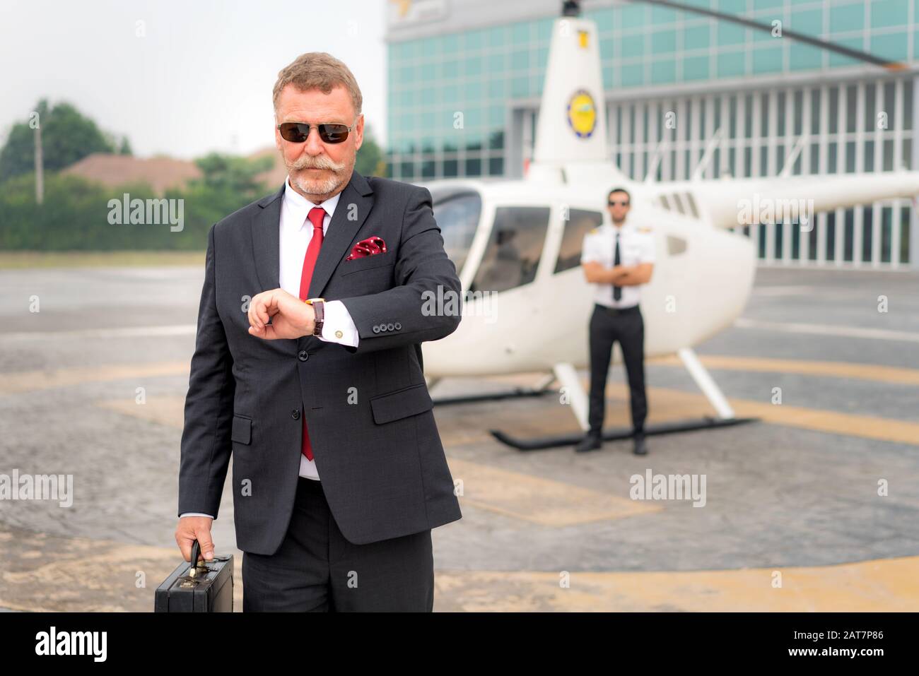 Uomo D'Affari anziano manager con orologio Briefcase watching per controllare l'orario in cui arriva a destinazione di eliporto in aeroporto con elicottero e captai Foto Stock