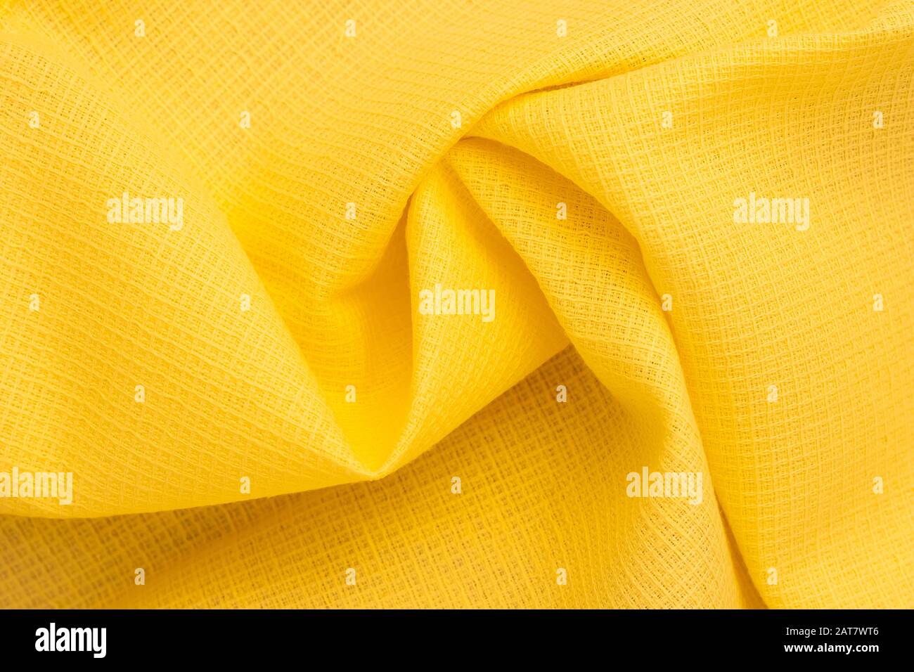 Sfondo astratto di tessuto giallo brillante. Pieghe, pieghe di tessuto di cotone. Modello del materiale, struttura del tessuto. Onde sullo sfondo Foto Stock