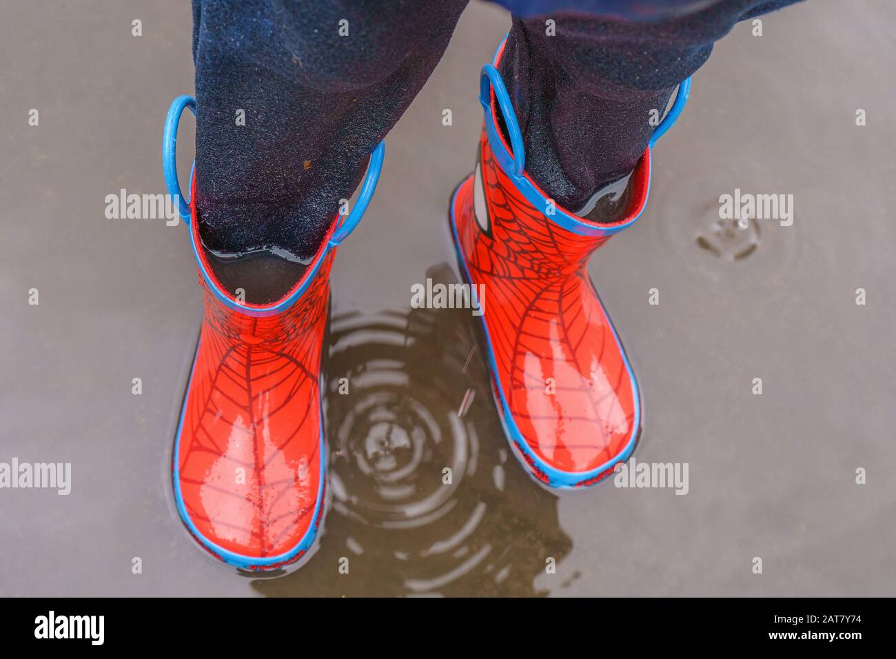 Il bambino che si tuffa in una pozza con i wellies pieni di acqua Foto Stock