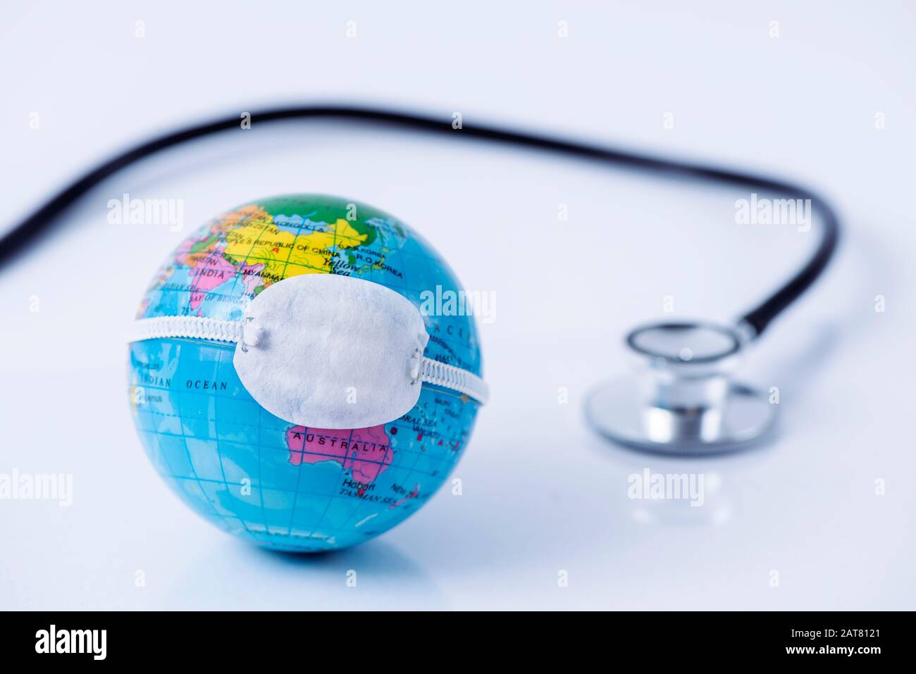 Primo piano di un globo terrestre con una maschera protettiva posta sulla Cina, raffigurante la recente epidemia di coronavirus, accanto a uno stetoscopio Foto Stock
