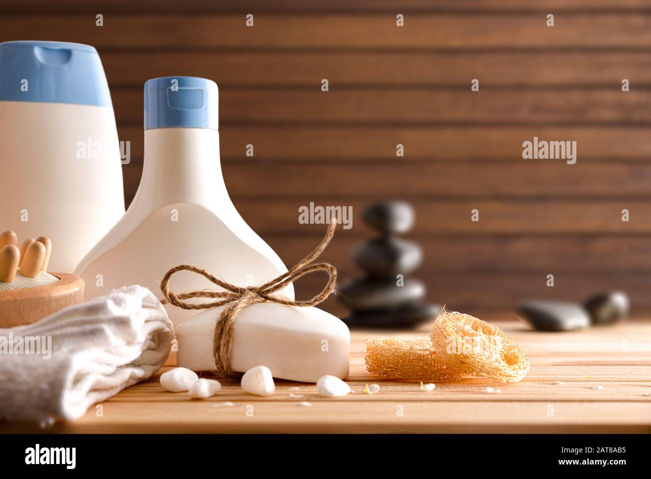 Massaggi e prodotti da bagno su tavolo in legno e pietre massaggianti con fondo in legno. Vista frontale. Composizione orizzontale. Foto Stock