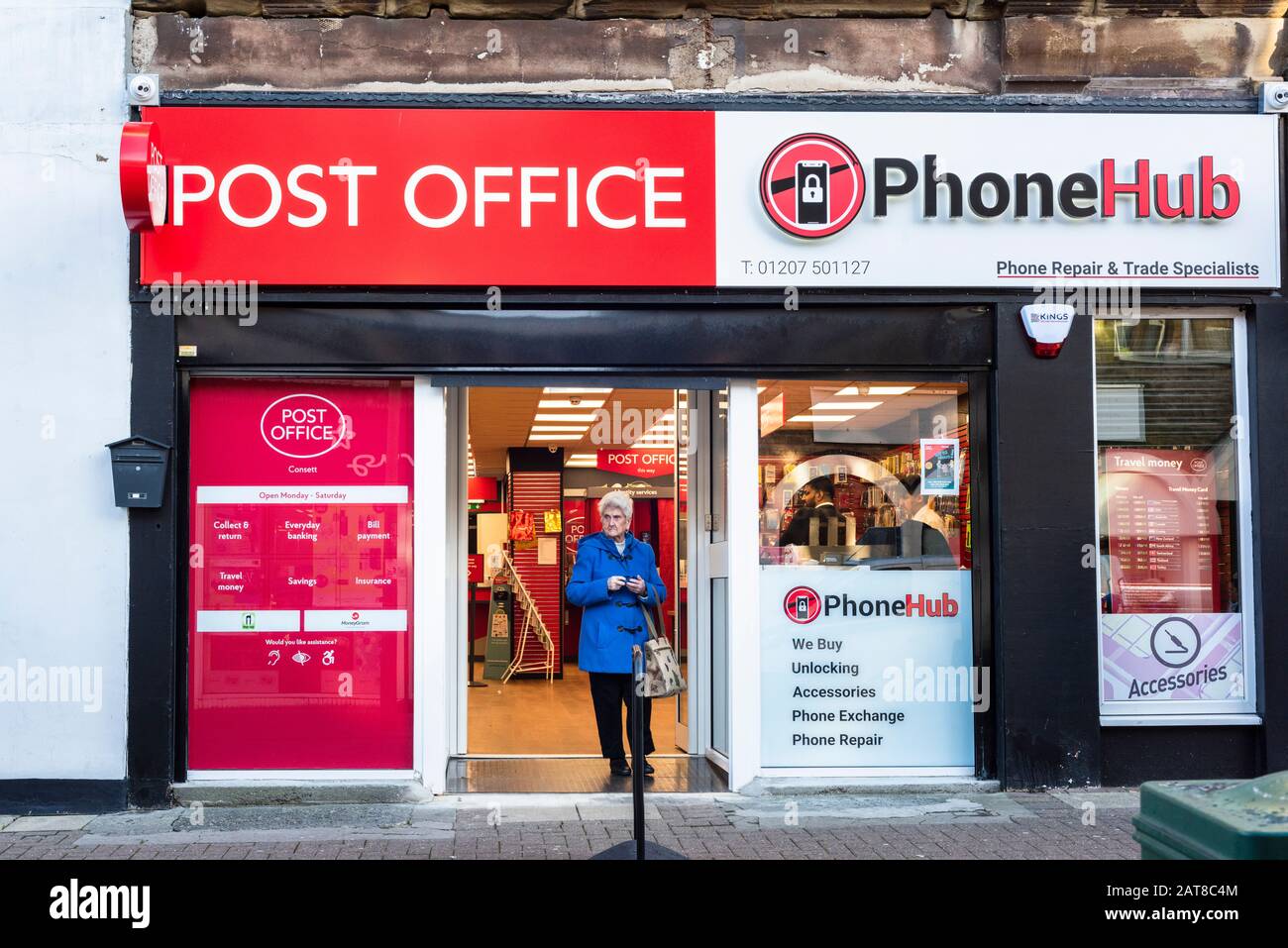 Donna anziana pensionato che lascia un negozio comune di uffici postali PhoneHub Foto Stock