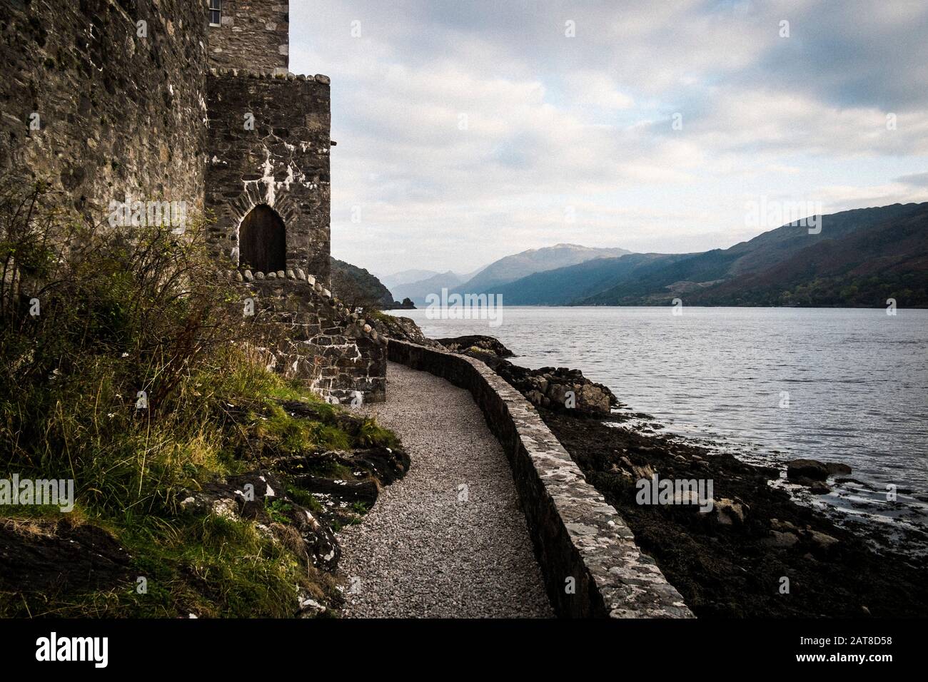 Castello in muro che si affaccia su un lago con montagne in lontananza. Foto Stock