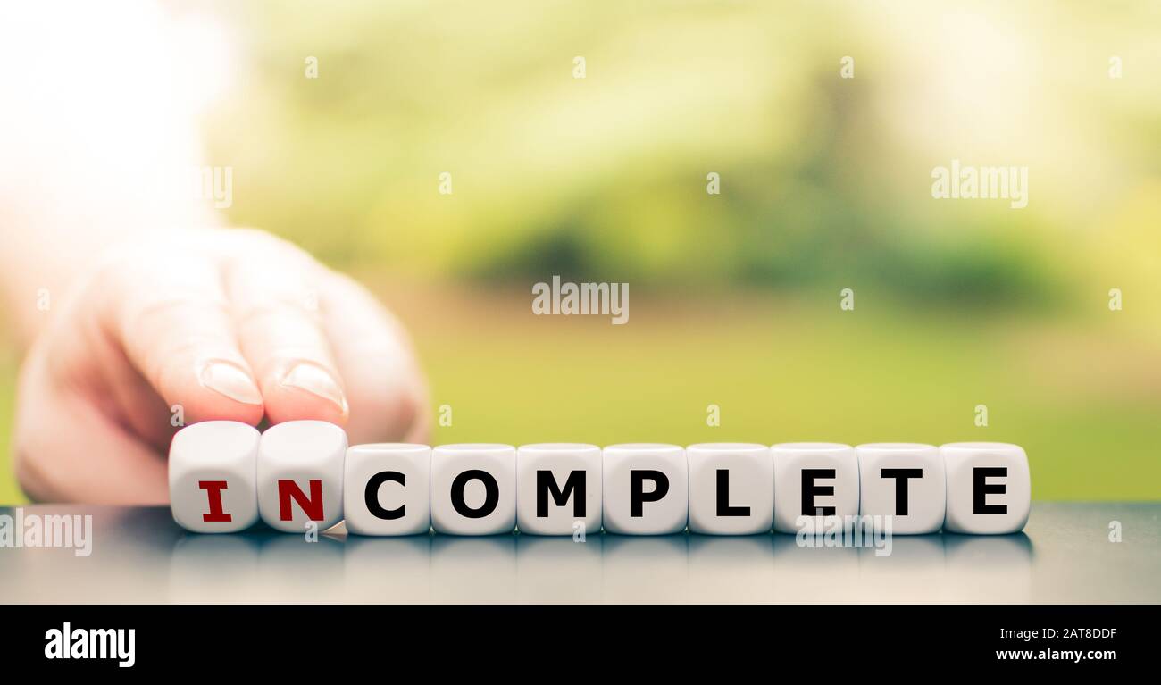 La mano gira i dadi e cambia la parola "incompleta" in "completa". Foto Stock