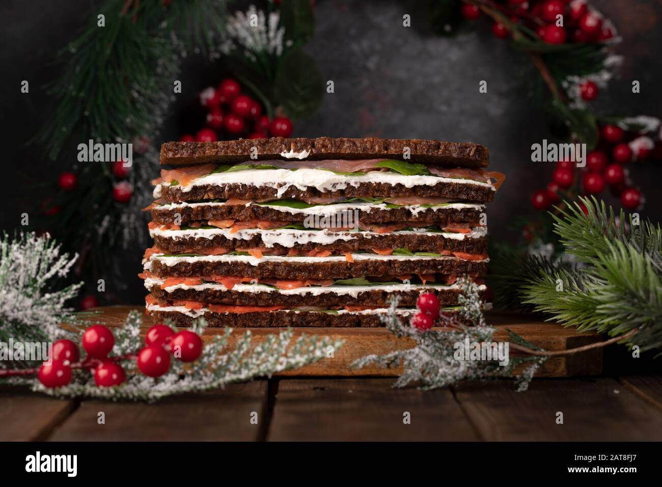 Torta di salmone composta da diversi strati alternati di pane di segale, formaggio cremoso, fette di salmone affumicato e foglie di spinaci, decorato per Natale. Foto Stock