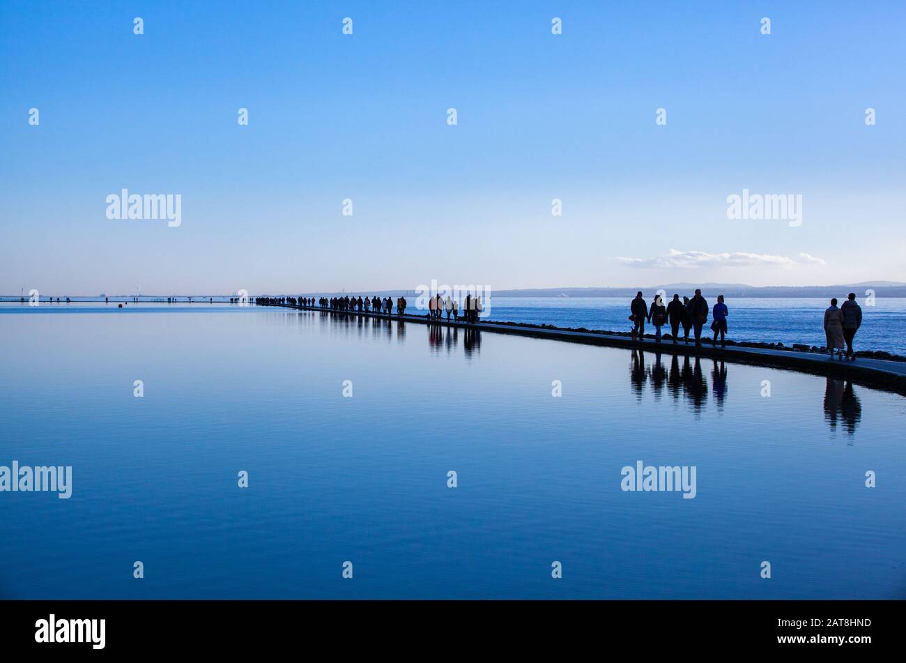 La gente che cammina intorno al lago marino a Kirby ovest sulla penisola di Wirral in inverno sul percorso della parete fra il lago di canottaggio e l'estuario di Dee Foto Stock