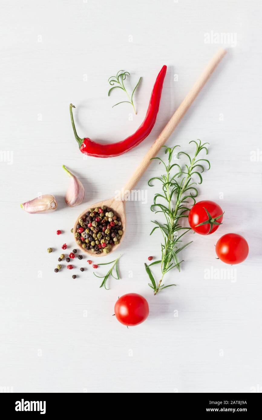 Composizione di colorati semi di pepe, peperoncino fresco, pomodori, aglio e rosmarino erbe vista dall'alto su sfondo bianco di legno. Erbe italiane e sp Foto Stock