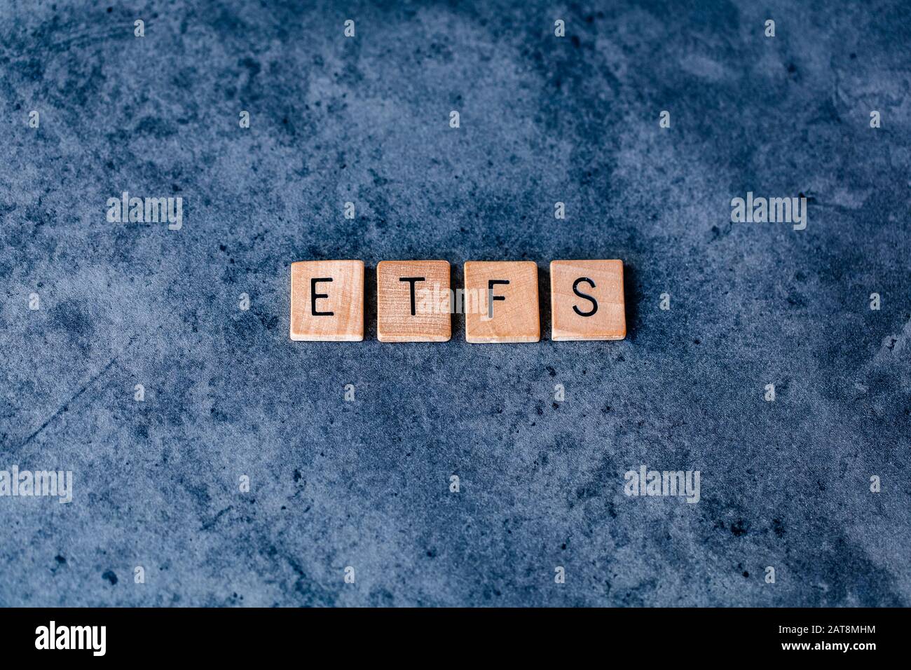 "ETFS" (fondi negoziati in borsa) scritto in piastrelle di legno su un fondo scuro e ruvido Foto Stock
