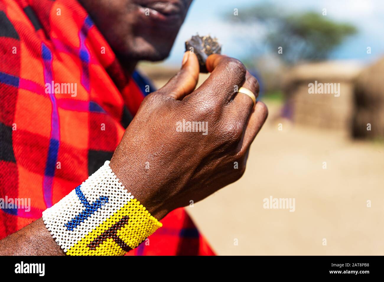 Uomo africano che tiene in mano una torta smoldering con bracciale colorato. Tanzania, Africa. Foto Stock