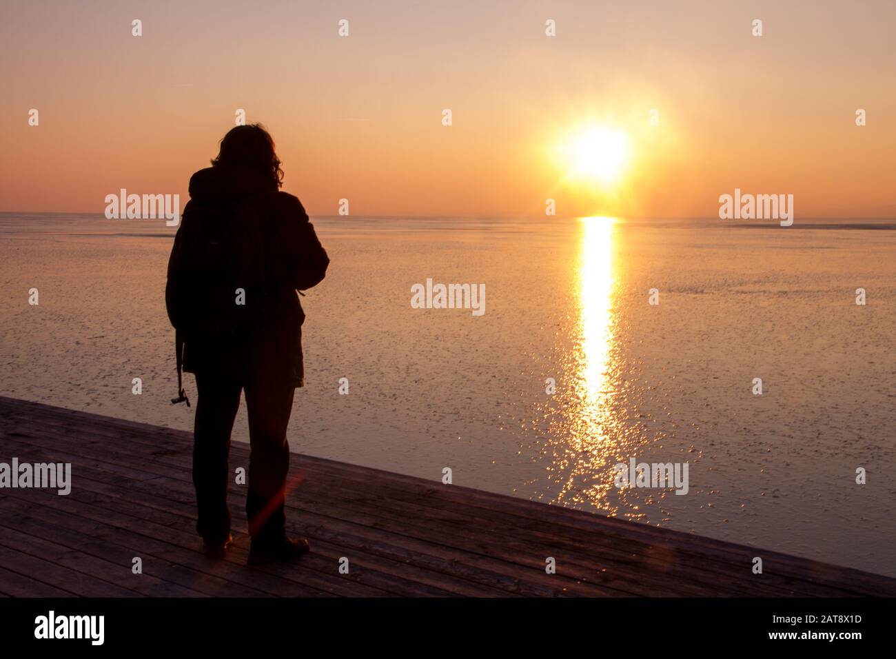 Uomo da dietro in piedi al lago durante il tramonto in inverno (Lago Neusiedl, Austria) Foto Stock